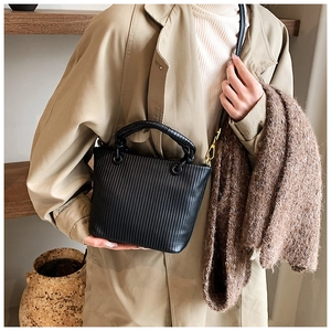 Close-up of black pleated bucket bag with gold hardware and woven circular handles