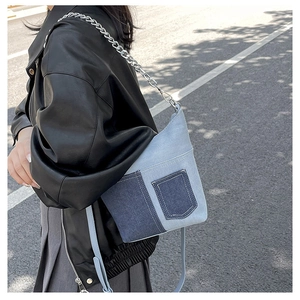 Detail of blue denim patchwork bag with silver chain strap on a leather jacket model