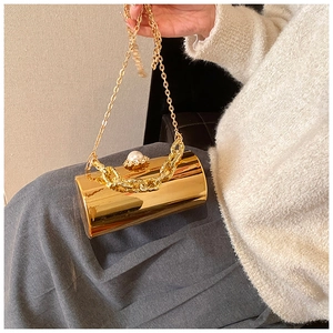 Detail of golden cylindrical evening bag with pearl clasp and metallic chain strap