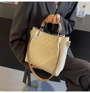 Detail of a beige quilted leather bucket bag with top handles and gold-tone hardware