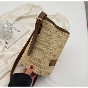 Detail of woven straw bucket bag with brown PU leather trim and adjustable gold buckle strap