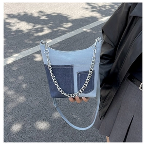 Chic blue denim bucket bag with silver chain strap shown in an outdoor street style setting