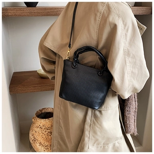 Detailed view of black pleated bucket bag featuring vertical texture and gold metal hooks