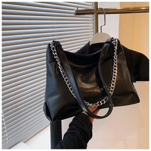 Detail of black glossy leather tote bag featuring a chunky silver metal chain strap