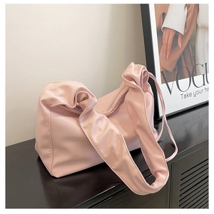Detail of light pink pleated cloud bag with wide knotted strap on a wooden surface