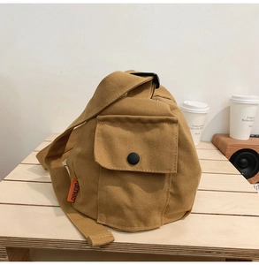 Détail du sac bandoulière en toile kaki avec poche avant et étiquette orange vive
