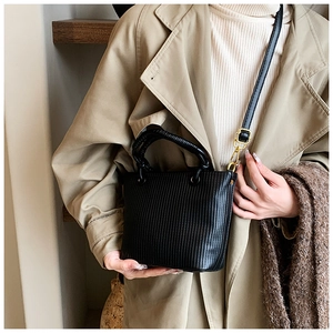 Detailed view of black pleated bucket bag with vertical texture and gold metal buckles