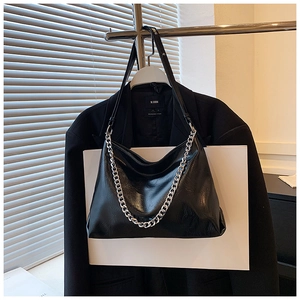Detail of black glossy leather hobo bag with silver chain strap and subtle pleated texture