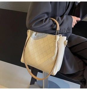Detail of cream quilted leather bucket bag with brown handles and golden hardware