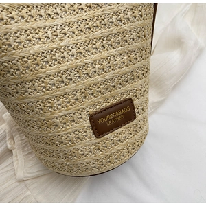 Close-up of woven straw bucket bag with dark brown leather brand tag and detailed texture