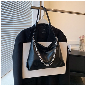 Detail of black glossy leather underarm bag with silver chain on a black blazer