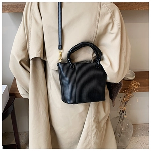 Lifestyle shot of black pleated bucket bag with twisted handle and gold hardware detail