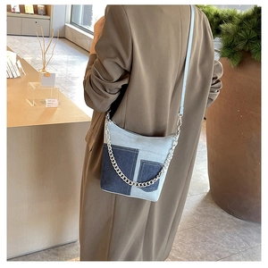 Detail of color-block denim crossbody bag with silver chain on model in brown coat