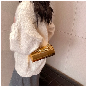 Close-up of golden mirror cylinder evening bag with thick chain handle on shoulder