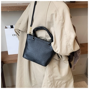 Detailed view of black pleated bucket bag with vertical texture and gold metal hardware