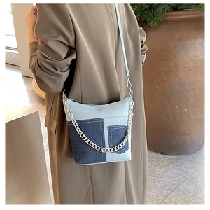Detail of blue denim bucket bag with metal chain decoration and patchwork design on model