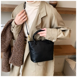 Detail of black vertical pleated bucket bag with gold hardware and slim shoulder strap