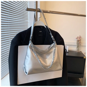 Detail view of silver metallic tote bag with chunky chain strap on a black blazer