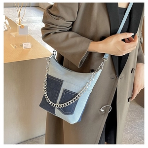 Detail of blue denim patchwork bucket bag with silver metal chain and leather strap