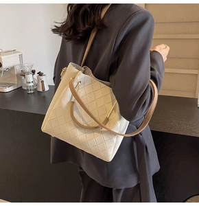 Detail of cream quilted tote bag showing brown leather handles and gold-tone hardware
