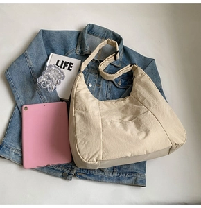 Minimalist beige nylon tote bag shown with daily essentials on a flat lay background