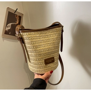 Detail of hand-woven straw bucket bag with dark brown leather trim and shoulder strap