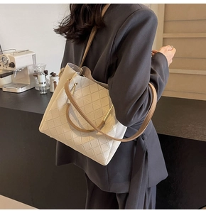 Detail of off-white quilted bucket bag with gold metal handle on a grey suit model