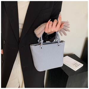 Close-up of light blue pleated bucket bag featuring metallic rings and knotted handle detail