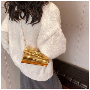 Detail of golden cylindrical evening bag with metal chains and pearl clasp on a model