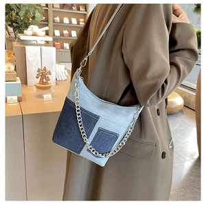 Detail of blue denim patchwork bucket bag with silver chains and front pockets worn by model