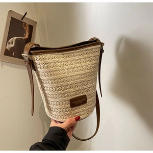 Detail of beige straw bucket bag featuring dark brown leather trim and a branded logo patch