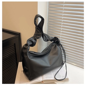 Detail of a black ruched shoulder bag with a pleated handle and side drawstring on a magazine