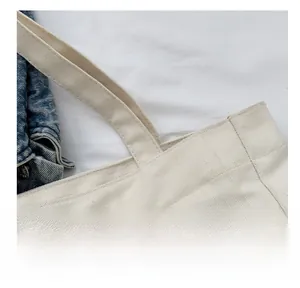 Detailed close-up of stitching on a cream canvas tote bag with reinforced handles