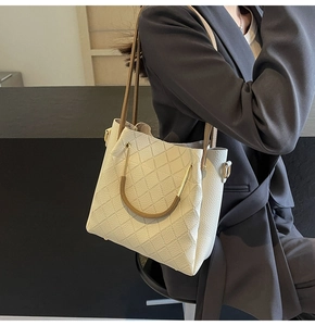 Detail of cream quilted leather bucket bag with gold hardware and brown straps on a model