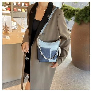 Detail of a patchwork denim shoulder bag with silver chain strap in a fashion setting