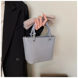 Detail of vertical pleated texture and woven handle on light gray fashion tote bag