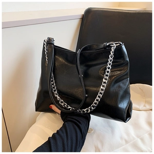 Detailed close-up of glossy black leather tote bag with thick silver metal chain strap