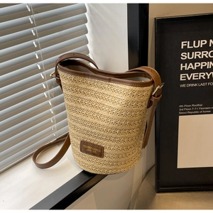 Close-up of beige woven bucket bag with brown leather trim and adjustable shoulder strap