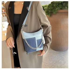 Detail view of light blue denim crossbody bag with silver chain on model in brown blazer
