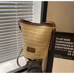 Detail shot of a woven straw bucket bag featuring dark brown leather trim and shoulder strap