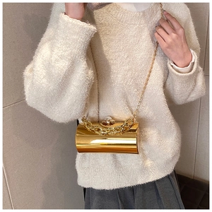 Detailed close-up of golden cylindrical evening bag with large pearl clasp and chain strap