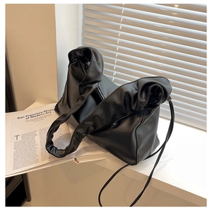 Detail shot of black ruched faux leather shoulder bag on a minimalist white windowsill