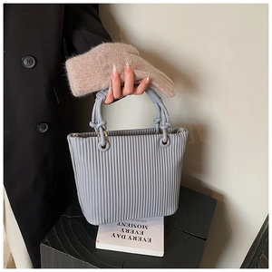 Detailed view of light blue pleated bucket bag with twisted handle on dark coat background