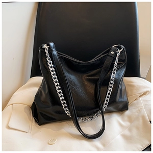 Detail of black glossy leather tote featuring silver chain strap and vintage texture