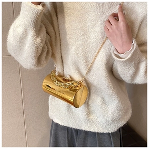 Close-up of golden cylinder evening bag with pearl clasp and chain strap on a model
