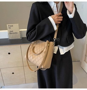 Detail of khaki bucket bag with quilted patterns and metallic handles on a model