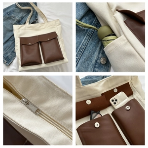 Detail view of canvas tote bag showing side pocket, leather flap pockets, and zip closure
