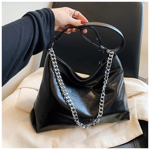 Detail of a black glossy leather tote bag featuring a stylish silver metal chain strap
