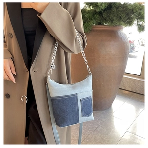 Detail of patchwork denim shoulder bag featuring silver metal chain and utility pockets