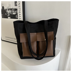 Close-up of black canvas tote bag featuring brown leather pockets and metal hardware detail